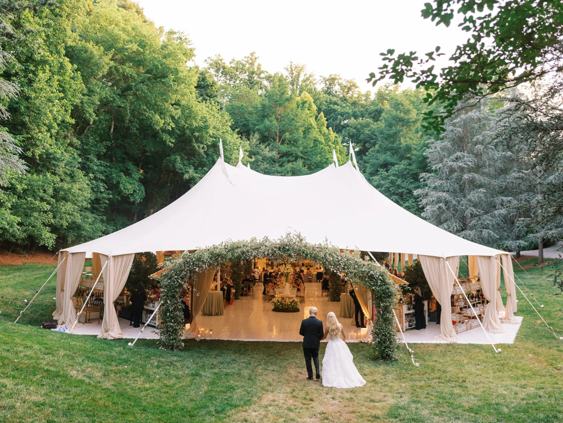 Couple walking toward a garden-arched wedding tent